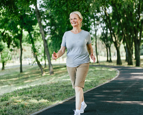 Smiling active senior woman jogging running and walking doing fitness in the park