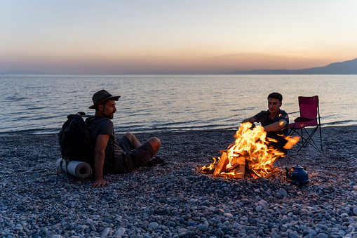 Young people camping by the sea. Enjoying camping at sunset. Tent and campfire.