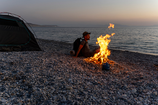 Young people camping by the sea. Enjoying camping at sunset. Tent and campfire.