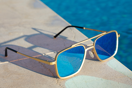 Mirrored sunglasses by a swimming pool reflecting the water