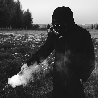 Man in black clothes wearing a gas mask and black smoke bomb in a field. The concept of ecological catastrophe or nuclear war.