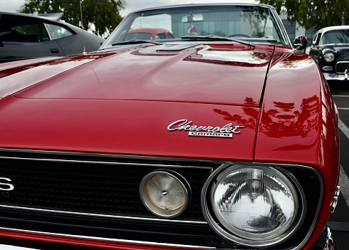 Fresno, United States – October 15, 2023: A vibrant red Classic Chevrolet Convertible Camaro at a car show Logo displayed across the body of the car