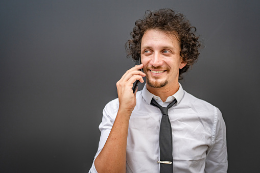 One caucasian man male businessman use smartphone mobile phone to make a call talk while stand outdoor wear white shirt happy confident success real person copy space