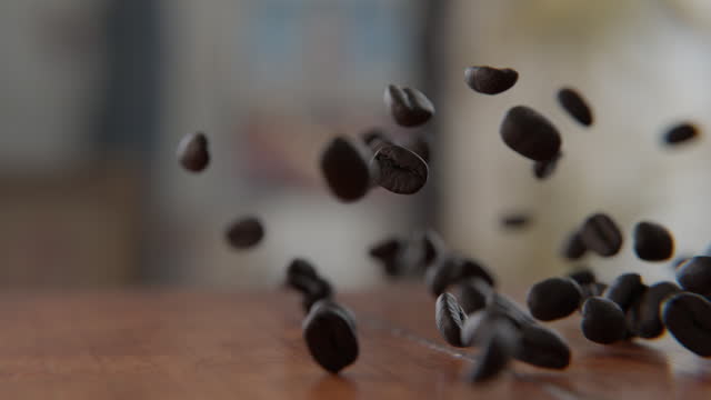 Coffee beans falling on and bouncing off of the wooden table