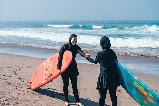 asian muslim woman greeting and talking prior surfing on the beach