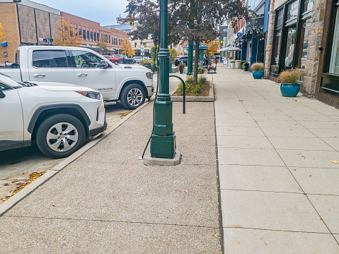 Sidewalk on old Woodward in Downtown Birmingham, Michigan on a cloudy autumn  day with white cars parked.