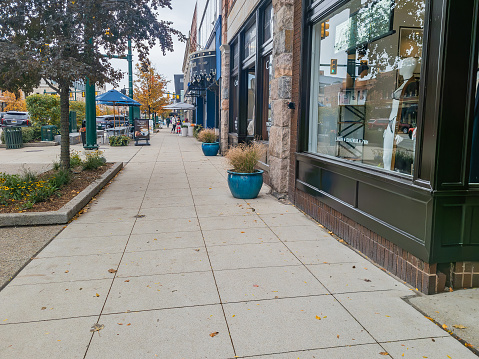 Sidewalk on old Woodward in Downtown Birmingham, Michigan on a cloudy autumn  day with white cars parked.