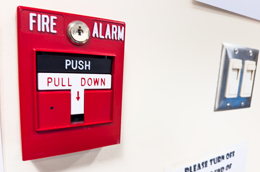A side angle view of a bright red fire alarm mounted on an office wall.