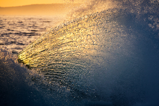 Ocean energy colliding and exploding into golden light forming a fan of water texture. Photographed in NSW, Australia.