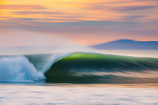 Motion blur of perfect wave breaking on beach with dramatic golden back light. Photographed in California.