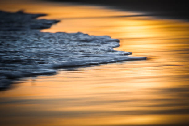 Blurred shutter speed of tidal movements on a shoreline reflecting a golden sunset.
