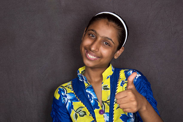 Cheerful Indian Girl wearing Blue Dress Sitting on Sofa Thumbs up. Isolated on Grey Background Landscape.