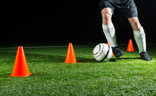 Soccer player is making a dribbling to get past some cones on a soccer field at night. He is practicing his skills. 