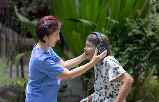 Senior woman  listening music on headphone with caregiver in backyard.