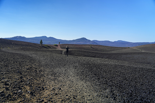 Female hiker standing on edge of crater taking photo of Cinder Cone in Lassen Volcanic National Park