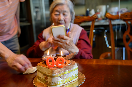 Senior woman taking smartphone photos of a cake celebrating her 90th birthday.