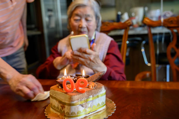 starsza kobieta robi zdjęcia smartfonem tortu z okazji swoich 90. urodzin. - one person lifestyles 80 plus years indoors zdjęcia i obrazy z banku zdjęć