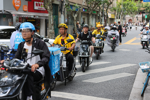 Shanghai, China - Aug 7, 2023: Delivery riders riding electric motor scooters in the streets in hot summer