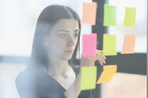 istock Concentrated woman puts colorful sticky notes on glass wall 1751387631