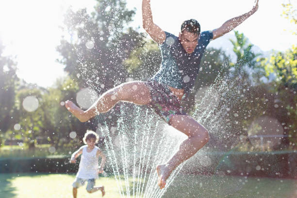 Happy small boy smiling and playing in water slide in the garden in the summer