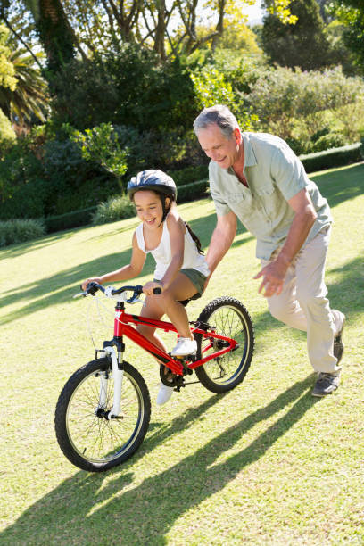 istock Older man teaching granddaughter to ride bicycle 175139231