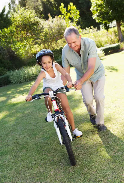 Photo of Older man teaching granddaughter to ride bicycle