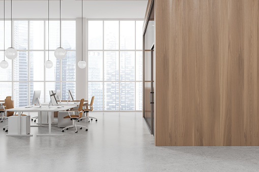 Interior of modern open space office with white and wooden walls, concrete floor, row of computer tables with beige chairs standing near panoramic window and mock up wall on the left. 3d rendering