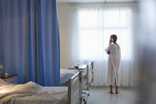patient in gown talking on cell phone in hospital room - examination gown zdjęcia i obrazy z banku zdjęć