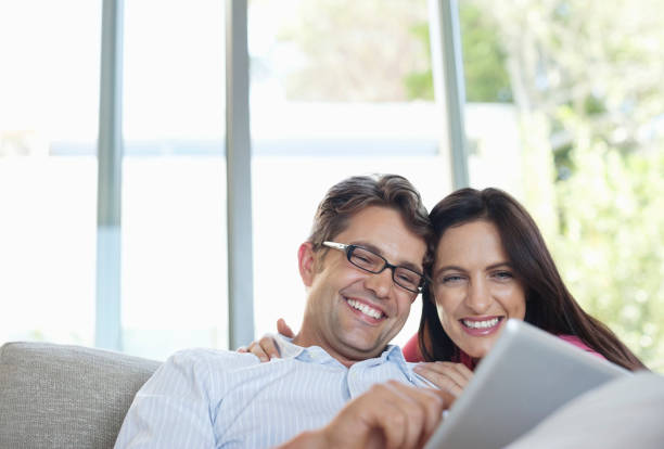 pareja con tableta en sofá - pareja de mediana edad fotografías e imágenes de stock