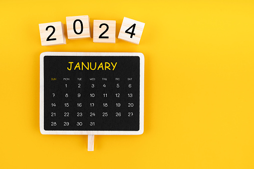 Calendar for January 2024 in black chalkboard with copy space on a yellow color background.
