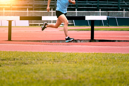 The feet of an athlete running outdoors at the racetrack. Fit young man is running on the race track. Male runner in sportswear running on stadium track with red coating outdoors.