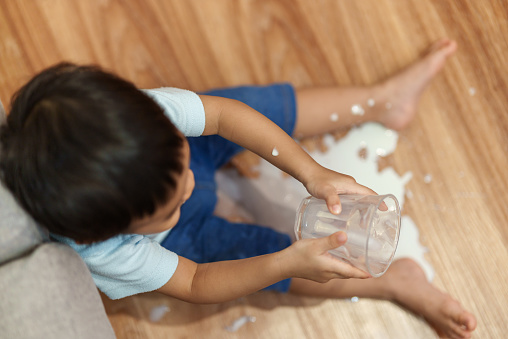Top view of Messy Asian little boy spilled milk all over the floor while drinking a glass of milk in living room at home.