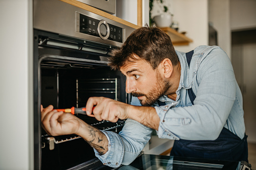Experienced male handyman seamlessly integrating a new oven into a kitchen setup, ensuring seamless functionality and efficient use for homeowners