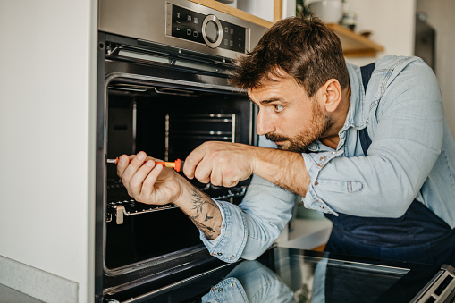 Experienced male handyman seamlessly integrating a new oven into a kitchen setup, ensuring seamless functionality and efficient use for homeowners