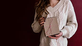 Banner. Faceless young woman in knitted white sweater holds Box gift in craft paper in hands