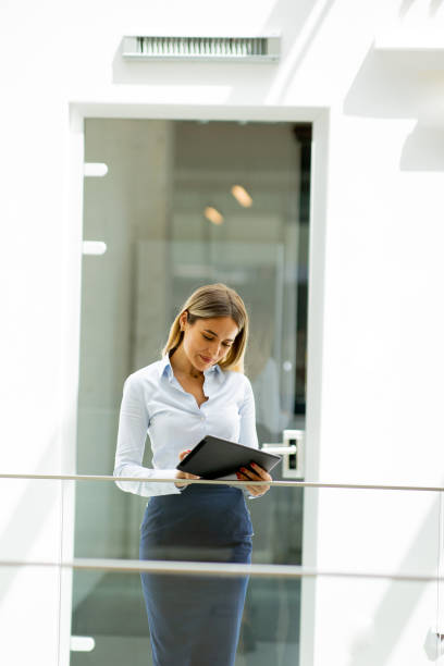 istock Young woman with digital tablet standing in the modern office hallway 1751564100