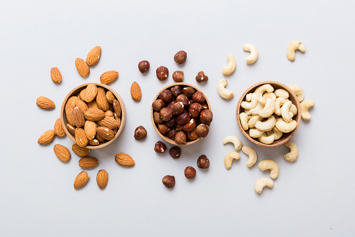 Assortment of nuts in wooden bowl on colored table. Cashew, hazelnuts, walnuts, almonds. Mix of nuts Top view with copy space.