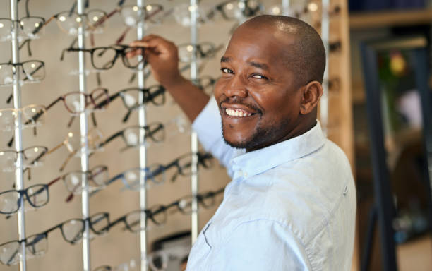 istock Black man, optometrist with glasses choice and vision in clinic or store for spectacles and shopping. Health, wellness and eye care, frame and prescription lens with cosmetic accessory and smile 1751594708