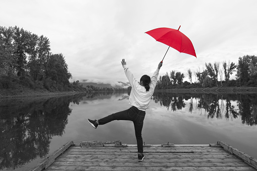 A concept digitally enhanced photo of a black and white photo of a woman standing on a dock holding a red umbrella by the Kootenai River in North Idaho.