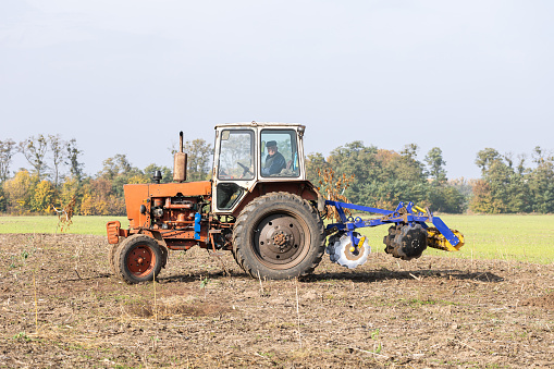 The tractor with a trailer for cultivating soil works on an agricultural plot.