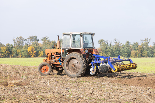 The tractor with a trailer for cultivating soil works on an agricultural plot.