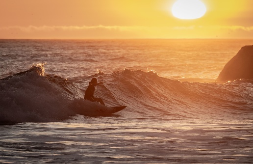 San Francisco, United States – October 08, 2023: A young man in a wetsuit surfing a large wave in Northern California against a beautiful sunset backdrop