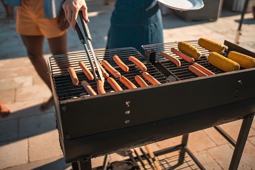 Close up on sausages and corn cobs on a grill at a villa pool party.