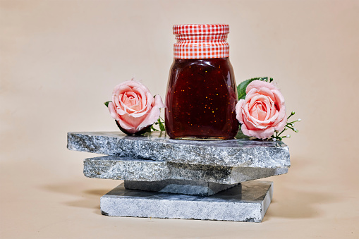 Fig jam in a glass jar on marble  podium or stone beauty with rose flowers. Product promotion showcase