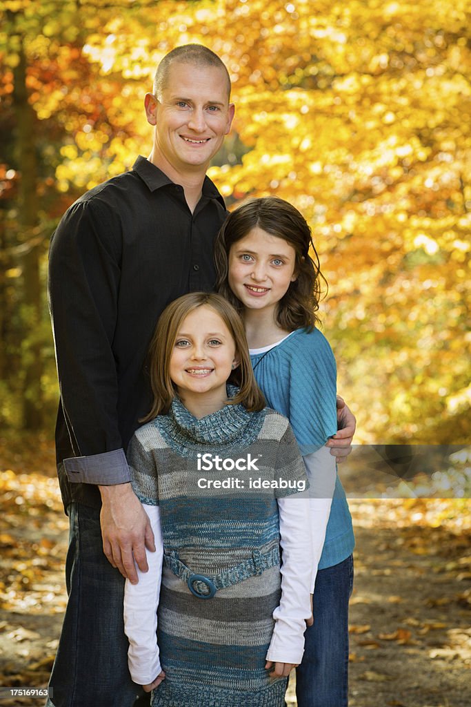 Portrait of Dad and Two Daughters, With Colorful Fall Woods Color image of a two little girls standing with their father outside on a beautiful autumn day. 10-11 Years Stock Photo