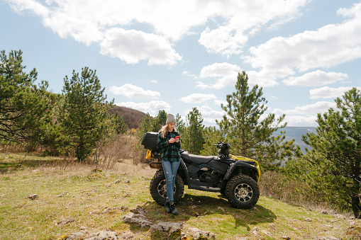 Photo of a young woman sitting on a quad bike and using maps application on mobile phone to search for a next adventure