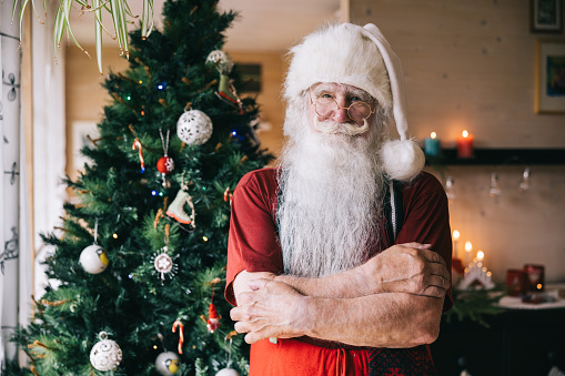 Santa Claus captured in the comfort of his home, with a beautifully adorned Christmas tree as a backdrop, exuding the spirit of the holiday season.