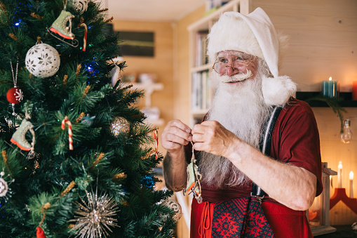 In the soft glow of Christmas lights, Santa Claus adds the finishing touches to a beautifully decorated tree, creating a sight to behold in the holiday season.