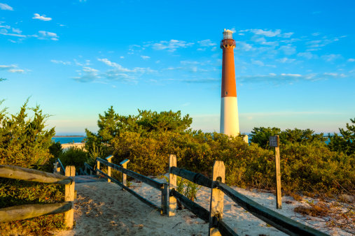 The Barnegat Lighthouse, also known as Old Barney, is located at Barnegat Light, New Jersey. A split rail fence guides the way along a sandy path to the 40-foot-tall red and white lighthouse which is accessible to tourists willing to climb its 217 steps. 