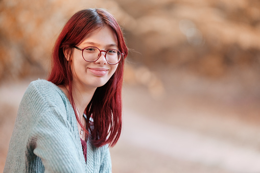 Portrait of a smiling red-haired teenage girl with glasses in a blue sweater.